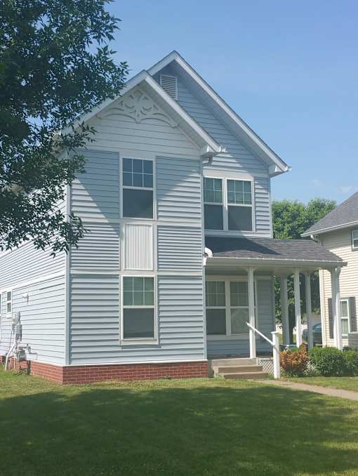 A white house with a porch and a red brick base.