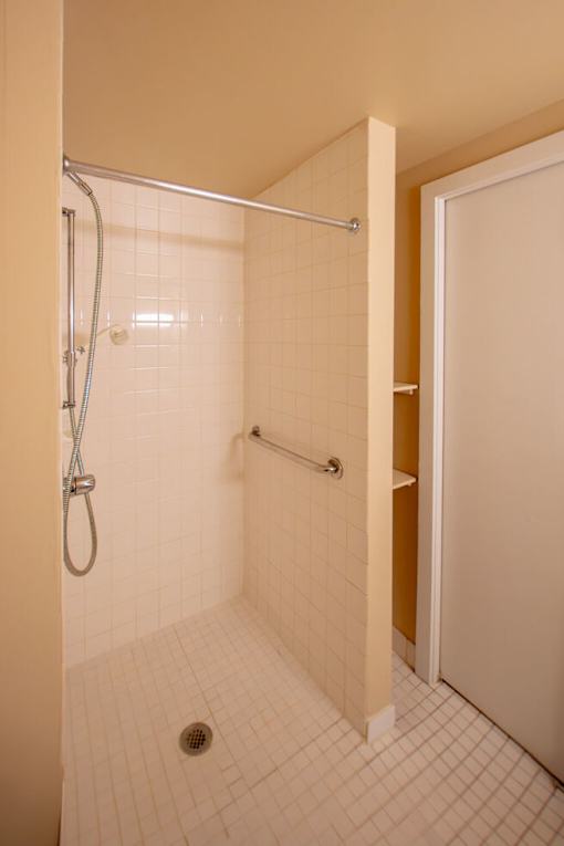 A white tiled bathroom with a shower and a door.