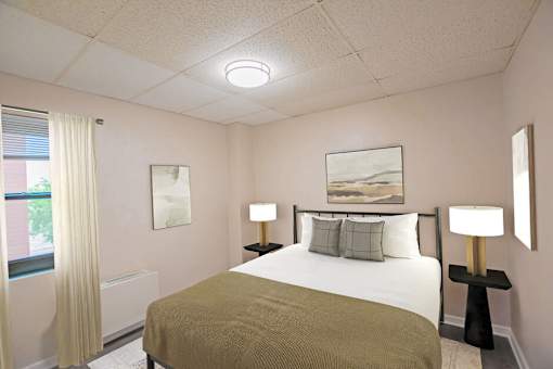 A bedroom with a bed, two lamps, and a painting on the wall.