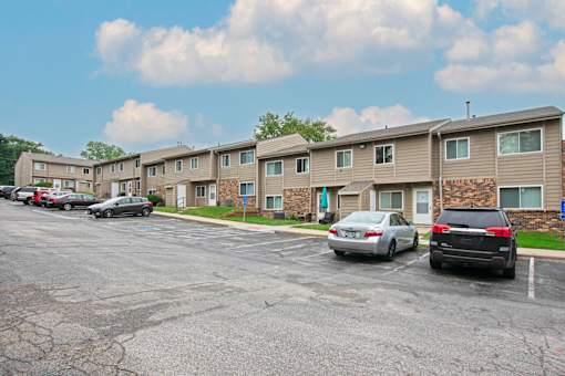 A parking lot in front of apartment buildings with cars parked.