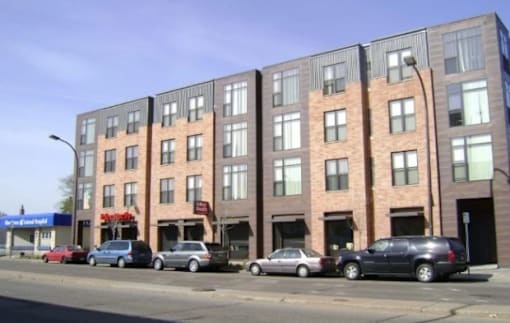 A row of apartment buildings with cars parked in front.