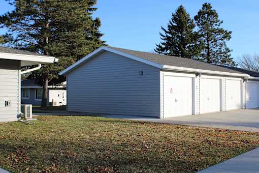A grey garage with a white door is situated in a grassy area.