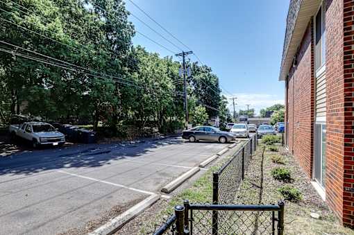 A street view with cars parked on the side and a brick building on the right.
