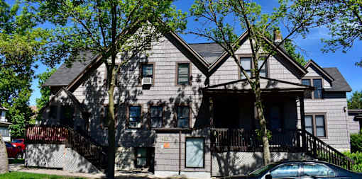 A grey house with a black balcony and a tree in front.