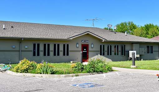 A building with a red door and a sign that reads "APT 304" is surrounded by a grassy area and a parking lot.