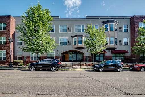 A black car is parked in front of a building with a red car parked behind it.