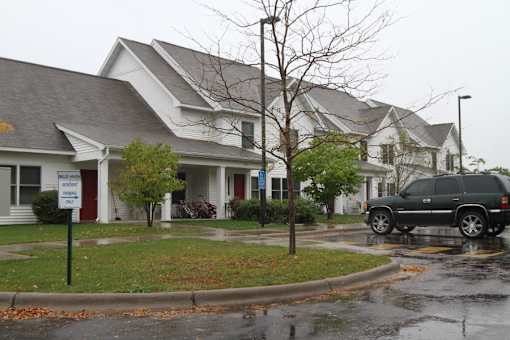 A wet street in front of a white house with a sign that says "Welcome to Woodland Heights".