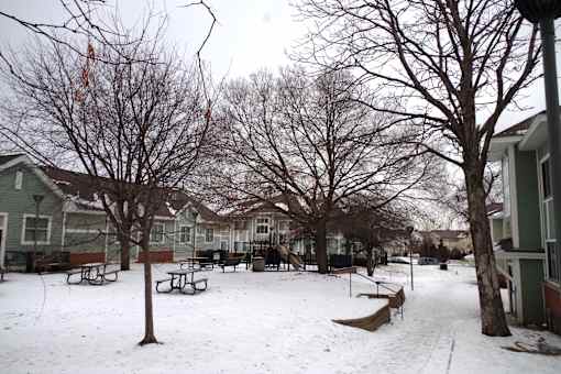 A snow-covered playground with a bench and a tree.