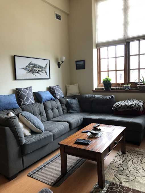 A living room with a grey couch, a wooden table, and a large window.