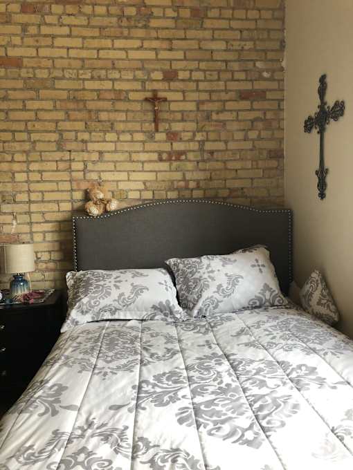 A bed with a grey and white comforter sits against a brick wall.