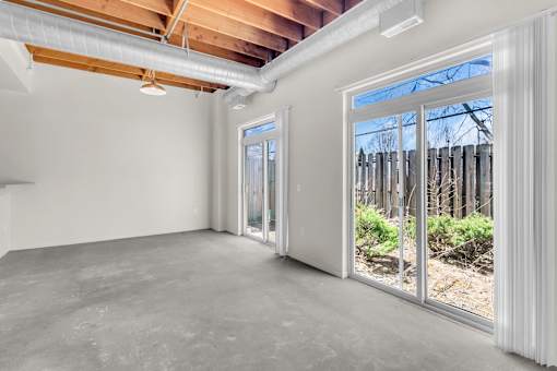 A room with a white wall and a window overlooking a fence.