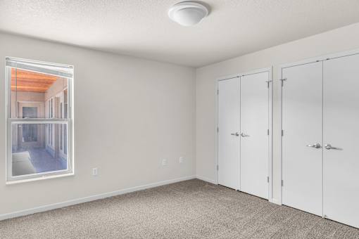 A room with white walls and carpeted floor with a picture on the wall and a window.