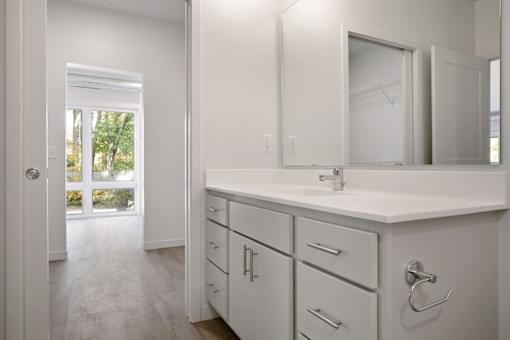 A white bathroom with a sink, mirror, and cabinets.