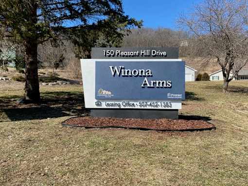 A sign for Winona Arms in front of a house.