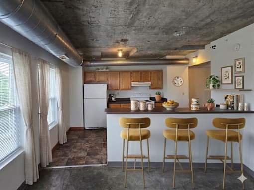 A kitchen with a white refrigerator and white cabinets with a bar area.