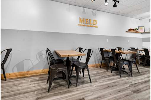 A dining area with chairs and tables in front of a wall with the word MELD on it.