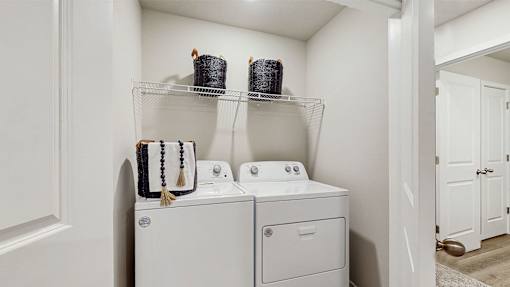 A white laundry room with a washer and dryer and a shelf above them.