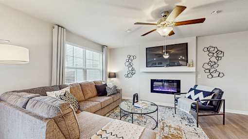 A living room with a couch, a chair, a coffee table, a fireplace, and a ceiling fan.
