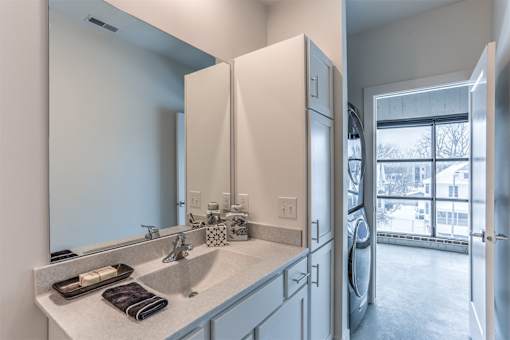 A bathroom with a sink, mirror, and a washer and dryer.