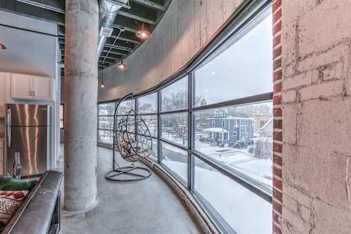 A view of a snowy landscape from a window in a room with a brick wall and a metal pole.