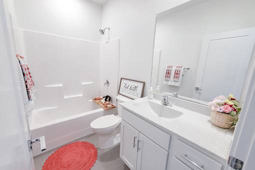 A white bathroom with a red rug and a white toilet.