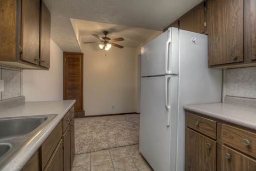 A kitchen with a white refrigerator, wooden cabinets, and a ceiling fan.