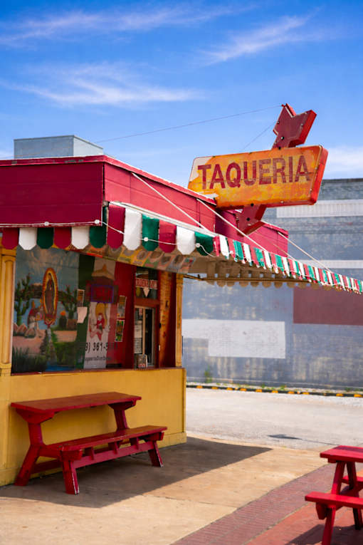 A red and yellow taqueria with a red bench in front.
