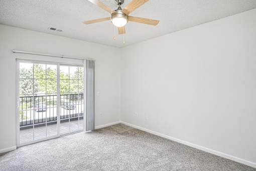 A room with a ceiling fan and a sliding glass door leading to a balcony.