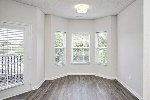 A room with a white ceiling, three windows with blinds, and a wooden floor.