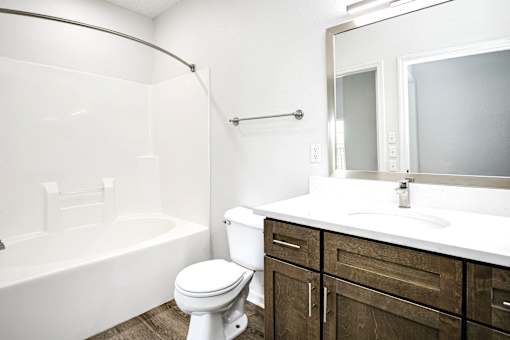A white toilet sits in a bathroom with a white tub and a white sink.