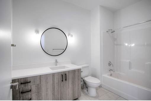 A bathroom with a white toilet, sink, and a round mirror.