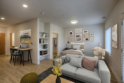 A living room with a grey couch and a desk with a laptop.