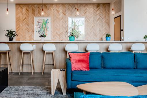 A blue couch with a red pillow sits in front of a wooden wall with a chevron pattern.