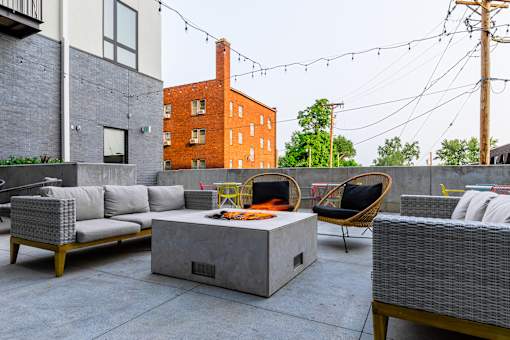 A patio with a grey couch, a yellow chair and a concrete table.