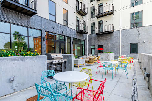 A patio with tables and chairs is surrounded by buildings.