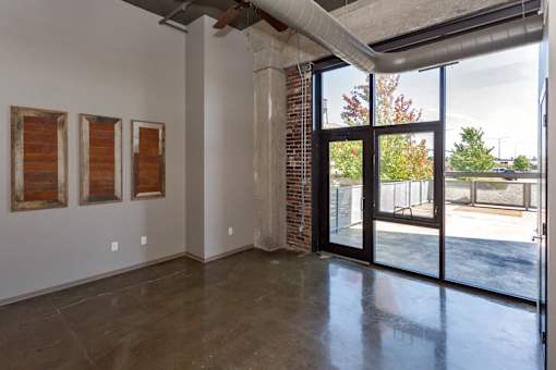 Three paintings hang on a white wall in a room with a concrete floor and a glass door leading to a parking lot.