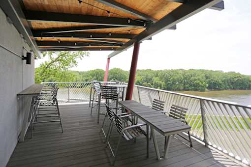 A wooden deck with metal chairs and tables overlooking a body of water.