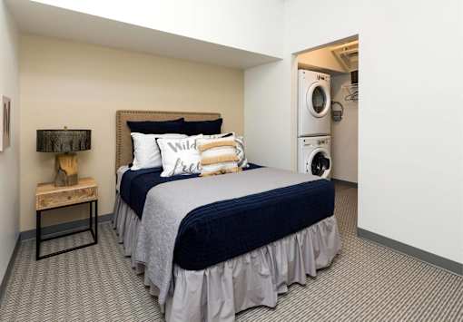 A bedroom with a bed, pillows, and a washing machine in the corner.