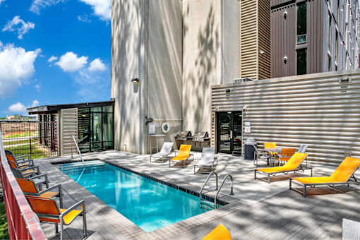 A pool with yellow chairs and a building in the background.
