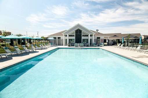 A large swimming pool in front of a building with a black fence and blue umbrellas.