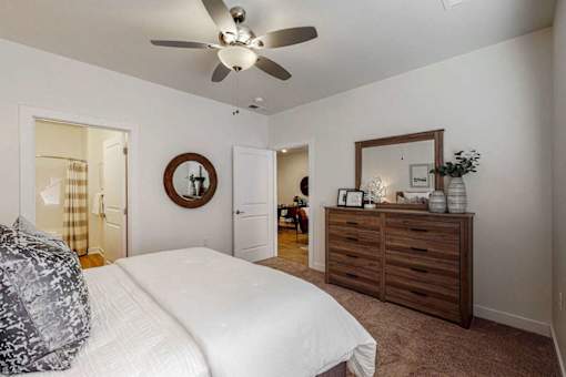 A bedroom with a bed, dresser, mirror, and a ceiling fan.