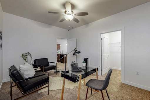 A living room with a black leather couch, a black glass table, and a ceiling fan.