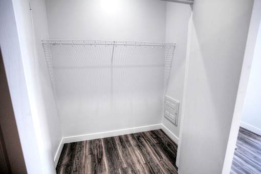 A white closet with a wood floor and a white shelf.