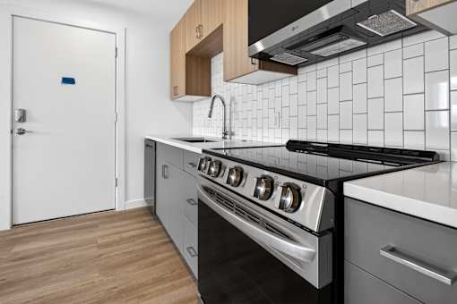 A modern kitchen with a white door, black stove, and wooden cabinets.