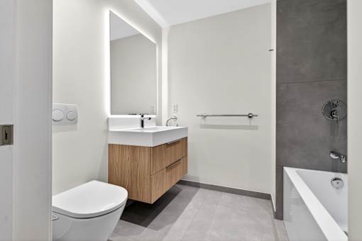 A modern bathroom with a white toilet, a sink with a wooden cabinet, and a white bathtub.