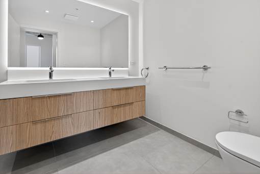 A modern bathroom with a large mirror, a sink with a vanity, and a toilet.
