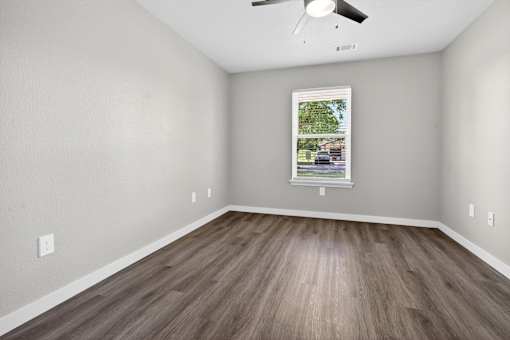 A room with a ceiling fan and a window showing a view of a street.