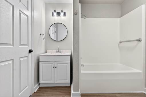 A white bathroom with a round mirror and a white bathtub.
