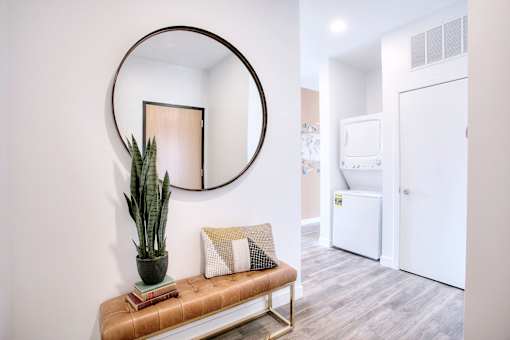A round mirror hangs on a wall above a bench with a potted plant on it.