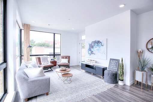 A living room with a grey sofa, a coffee table, a grey ottoman, a painting, a plant, and a mirror.